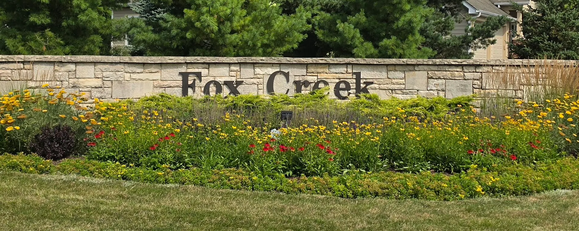 The landscaped Fox Creek entrance monument with homes and trees behind it