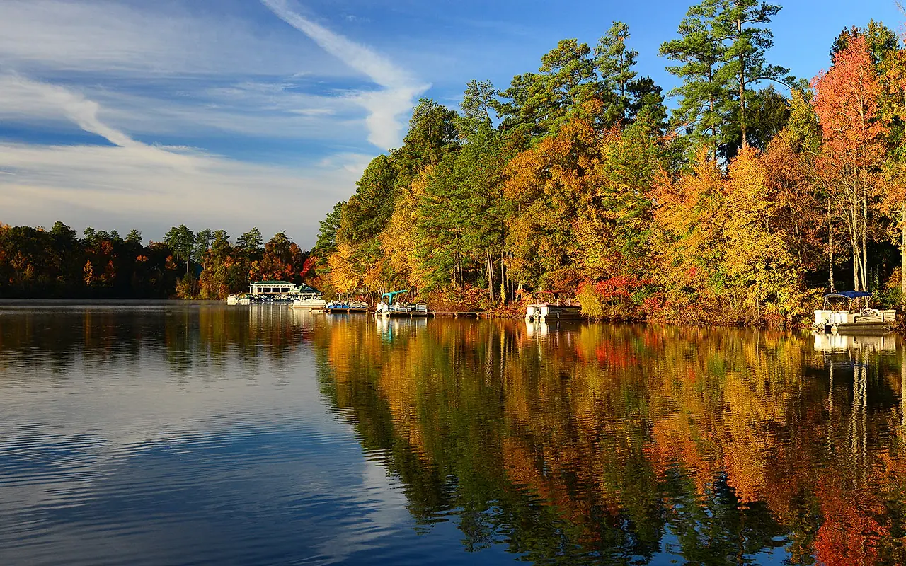 Woodlake shoreline, boats, and autumn trees reflected in Swift Creek Reservoir